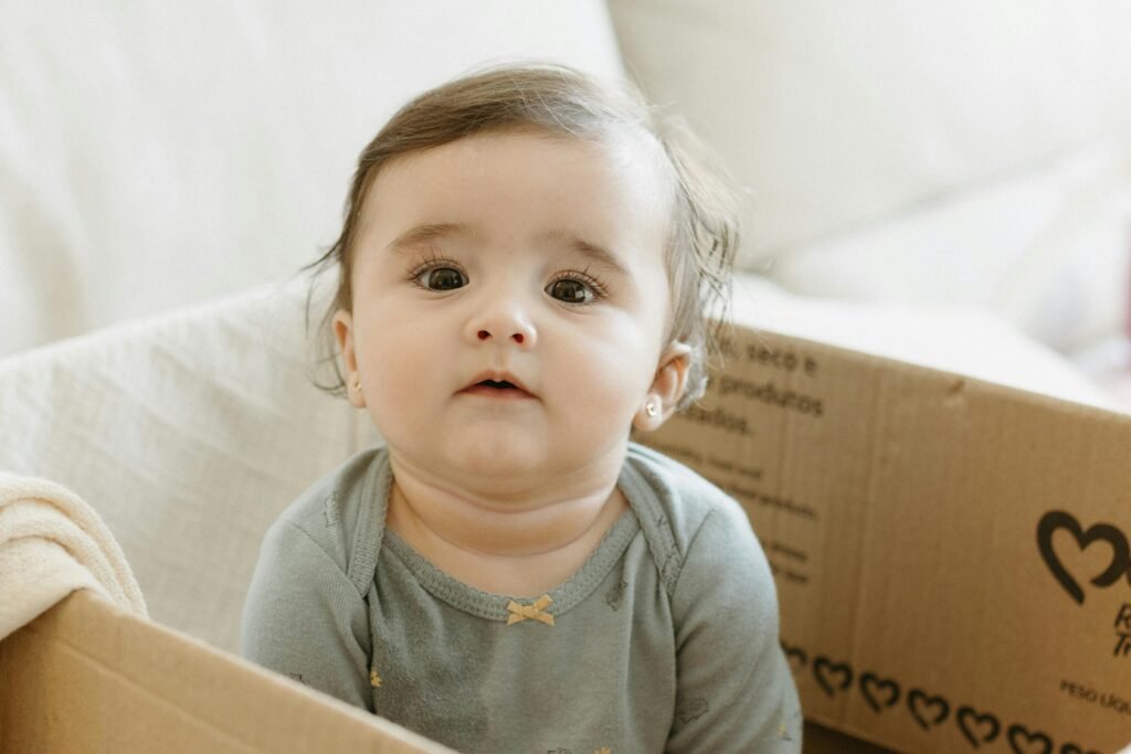 Charming portrait of a baby sitting in a cardboard box indoors, captured with soft lighting.